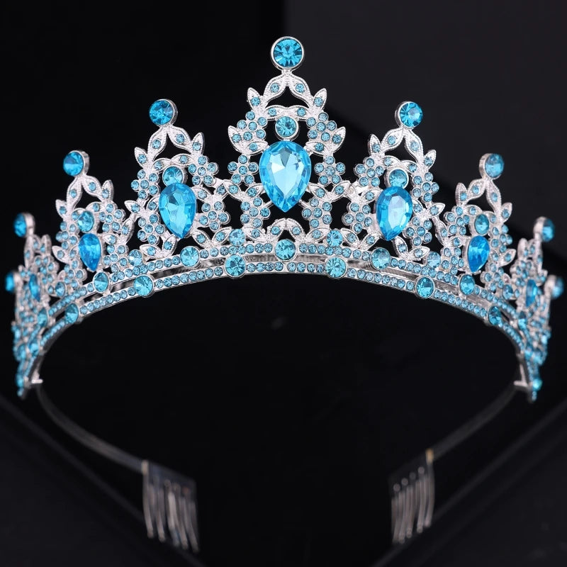 A sparkling silver tiara adorned with intricate patterns of round and teardrop-shaped blue gemstones, set against a black background, showcasing elegance and luxury.
