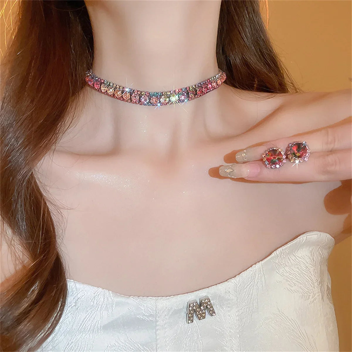 Woman wearing a sparkly choker necklace and matching earrings, showcasing jewelry. Her white, textured strapless dress features a small "M" brooch. Her hair is long and brown.