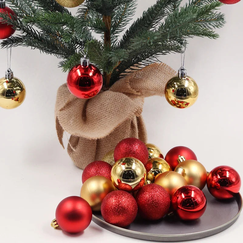 A small Christmas tree wrapped in burlap features red and gold baubles. A cluster of similar baubles rests on a gray plate beneath the tree.