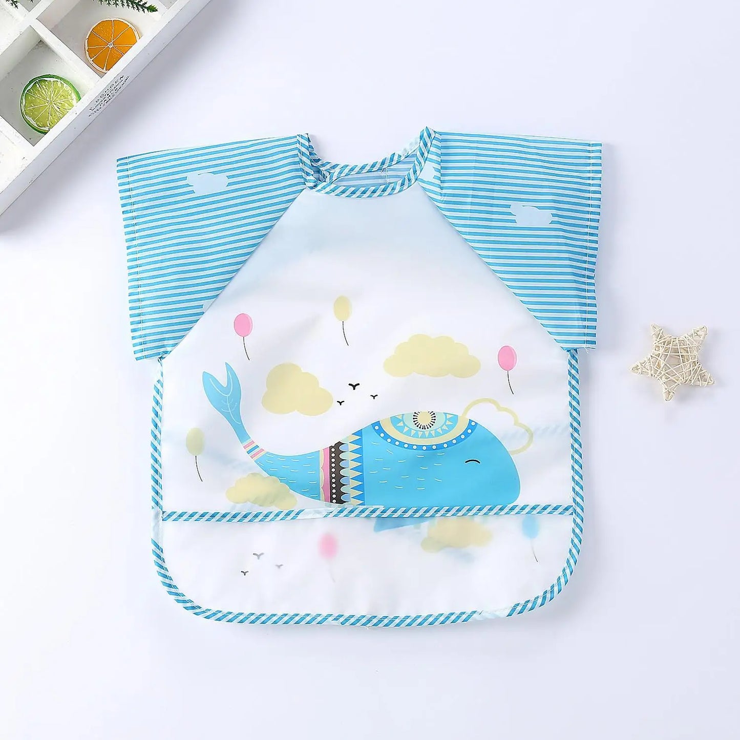 Blue and white striped baby bib featuring a playful whale design surrounded by clouds and balloons. A star-shaped ornament lies to the side on a white background.