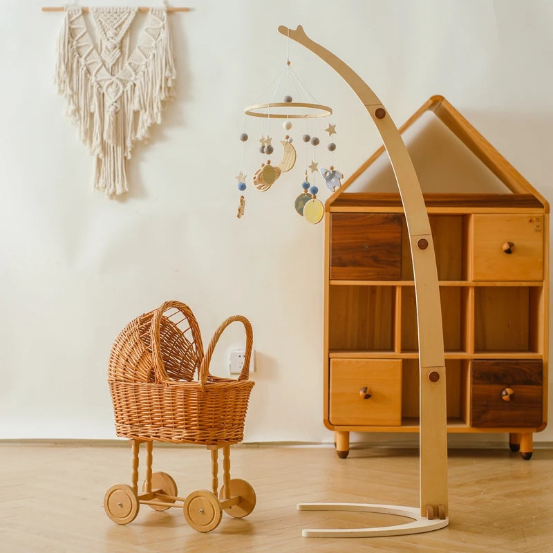 A cozy nursery features a wicker stroller, a wooden cube shelf, and a macramé wall hanging. A hanging mobile with stars and moons adds a whimsical touch.