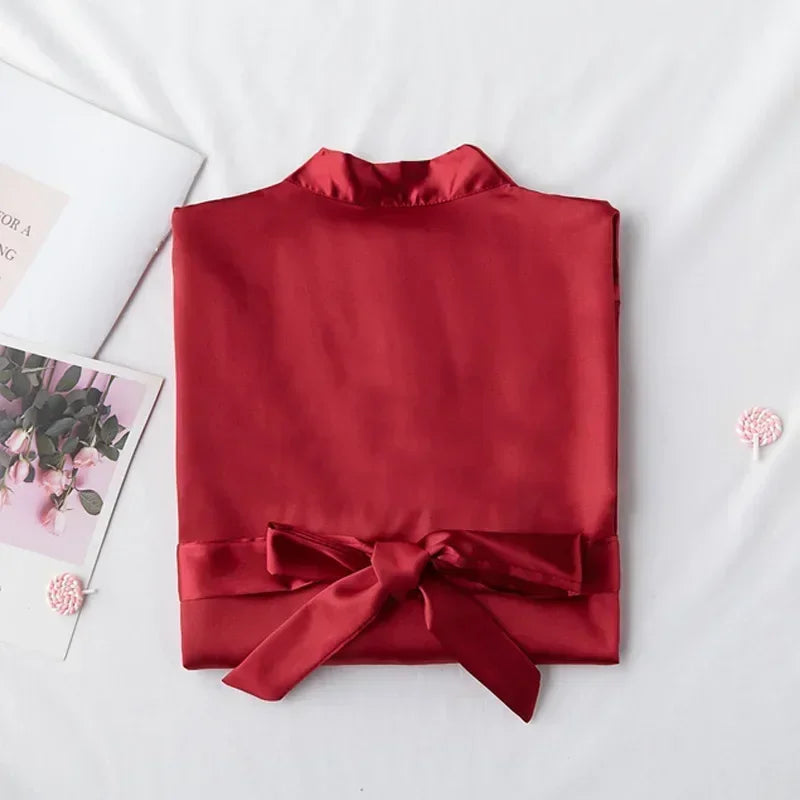 Folded red satin jacket with a tied bow, placed on a white surface. Nearby are a floral magazine and delicate pink decorations.