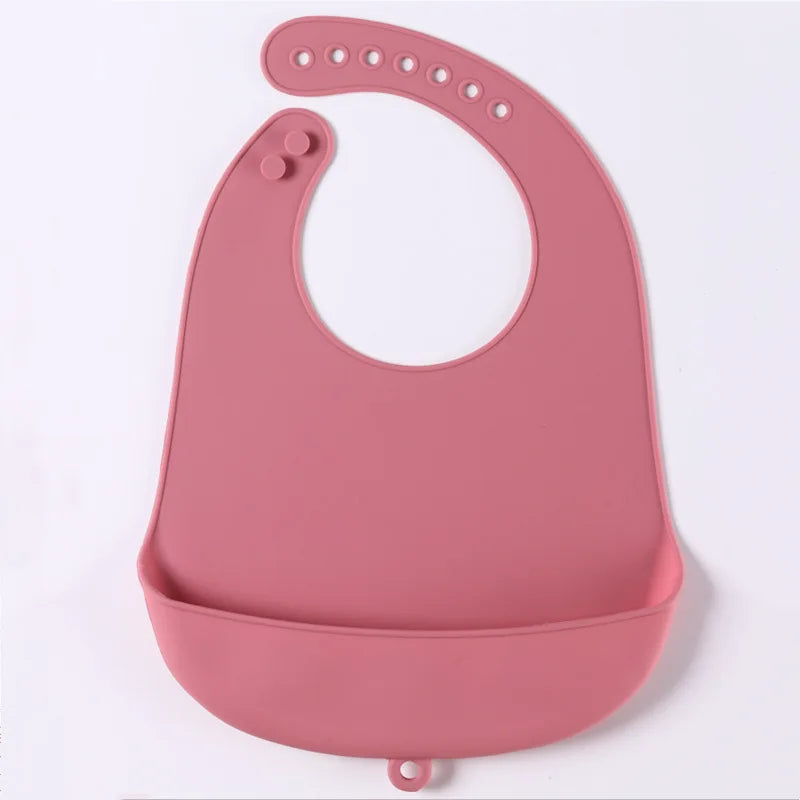 A pink silicone baby bib with adjustable strap and snap buttons, featuring a wide pocket at the bottom to catch food.