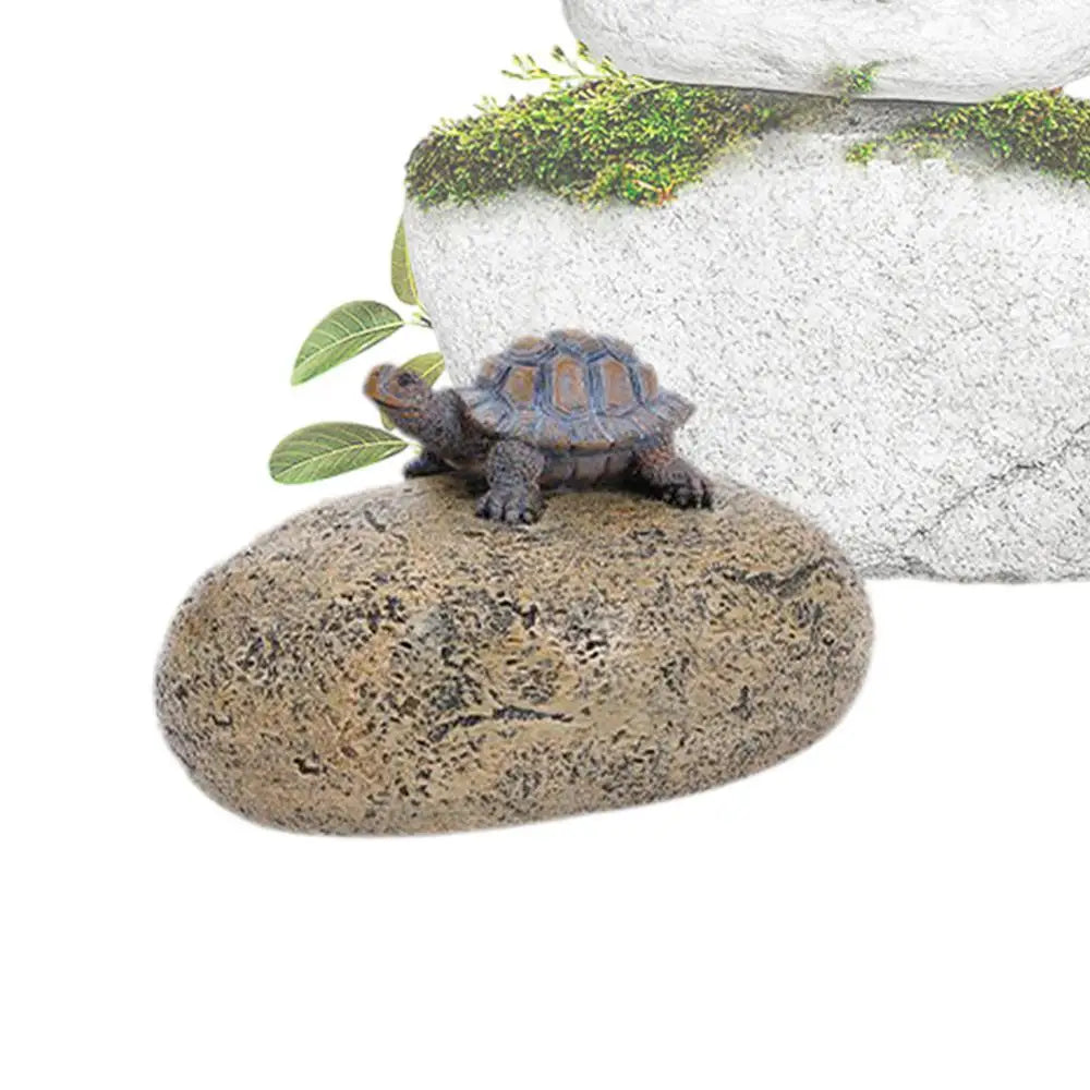 A small tortoise resting on a textured brown stone. The background features green leaves and a larger stone topped with moss, creating a natural setting.