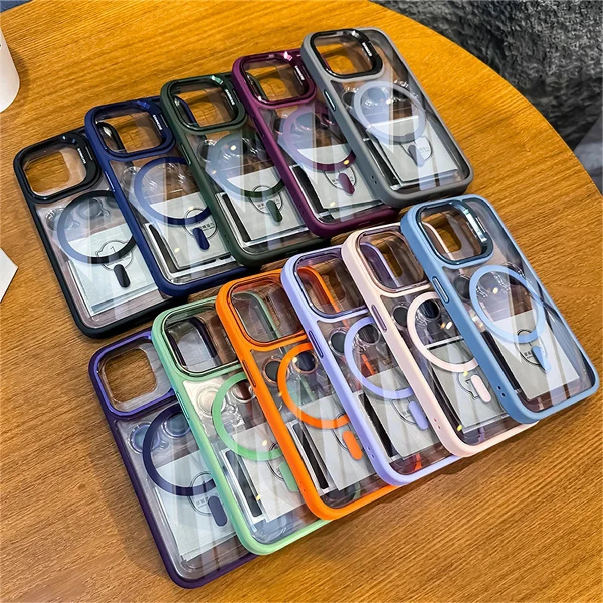 Ten transparent phone cases with colored edges are arranged in two rows on a wooden table. Each case has built-in ring holders in various shades like purple, green, orange, and blue.