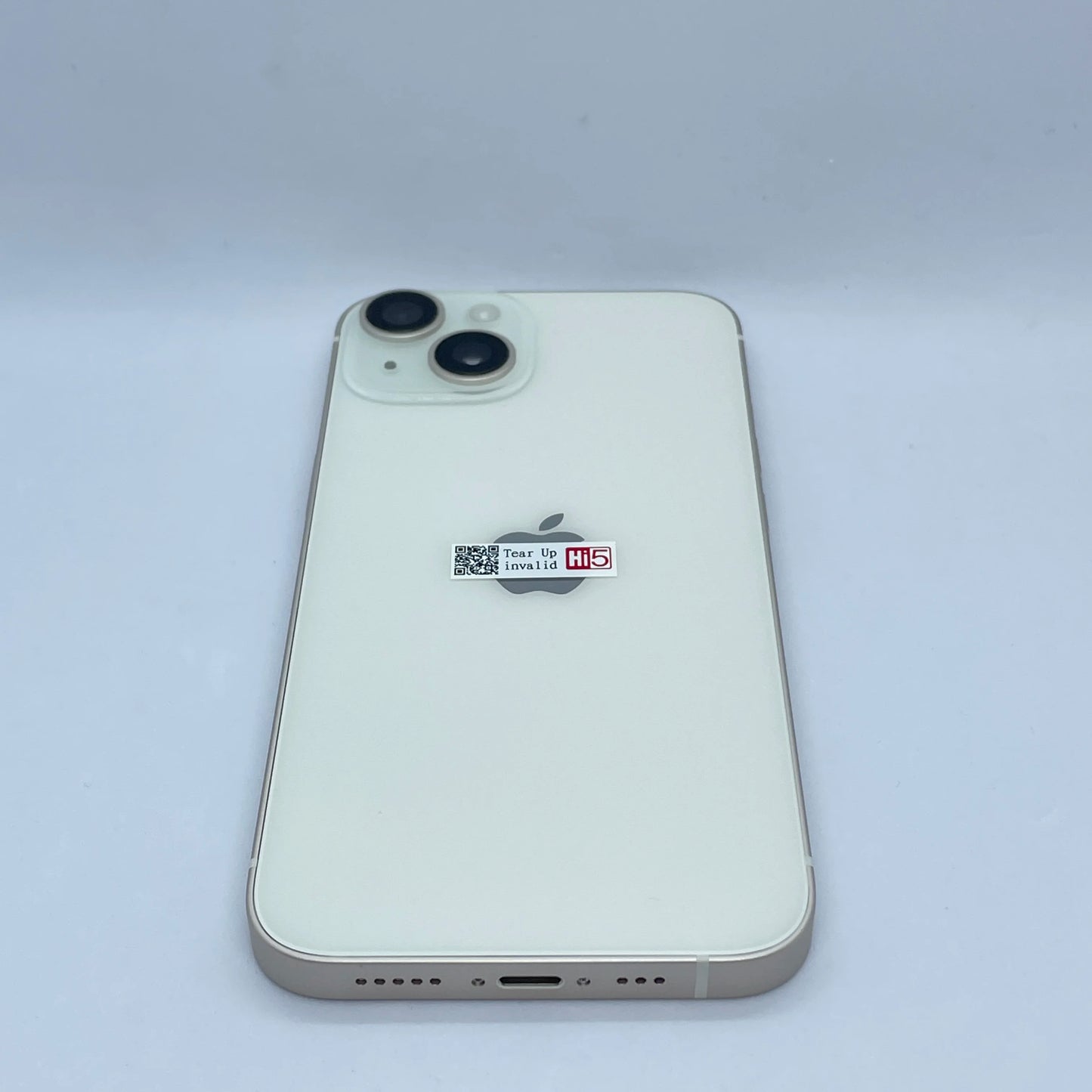 White smartphone with dual cameras on the back, featuring a small sticker above the central logo. The device rests on a plain white background.