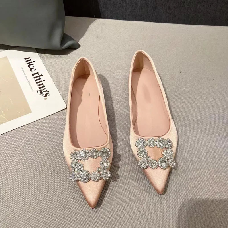 Elegant beige pointed-toe flats with sparkling rhinestone buckles are displayed on a gray surface. A magazine titled “nice things.” partially visible beside them.