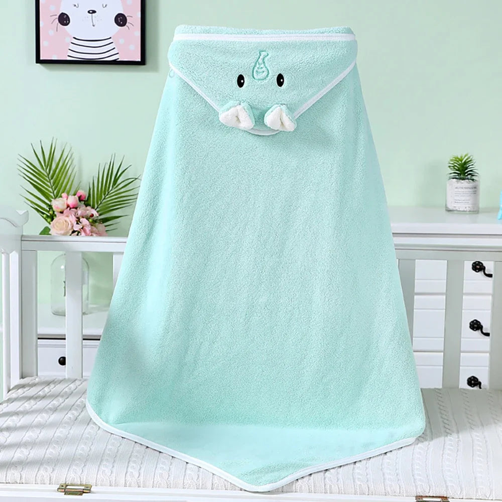 A soft mint green baby towel with an elephant face design and trunk, displayed on a crib. The room is decorated with a drawing of a cat, plants, and pink flowers.