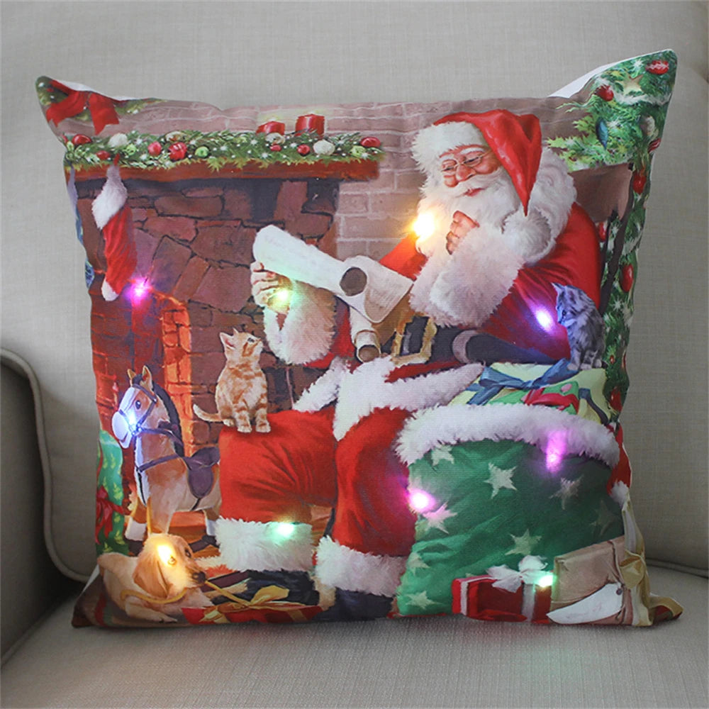 Festive pillow featuring Santa Claus by a fireplace, reading a list, with a kitten, horse toy, and presents. Colorful LED lights enhance the cozy holiday scene.