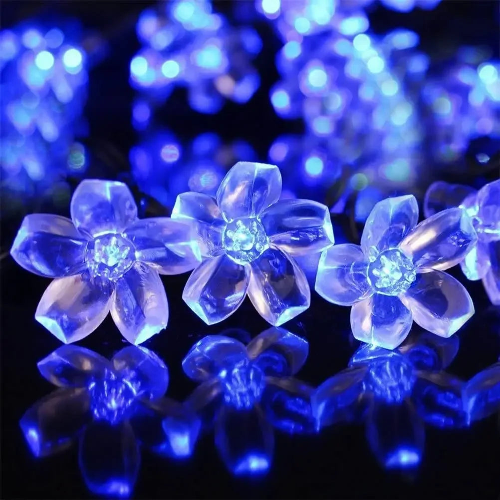 Glowing blue LED flowers with five petals, arranged in close-up on a reflective surface, creating a vibrant and luminous effect with blurred lights in the background.