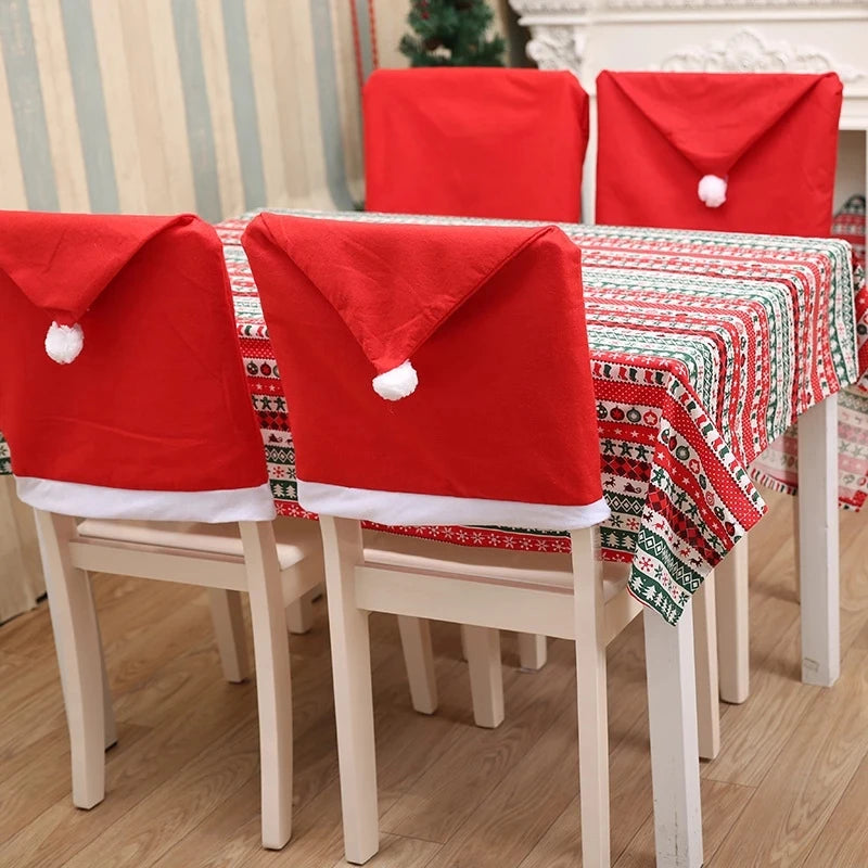 Chairs covered with red Santa hat chair covers surround a table adorned with a festive red, green, and white patterned tablecloth in a room with light wood flooring.