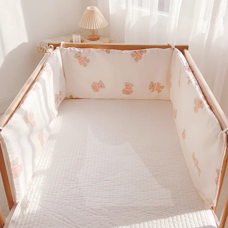 A wooden crib with white bedding and teddy bear-patterned bumpers. Soft sunlight filters through sheer curtains. A small table with a lamp is in the corner.