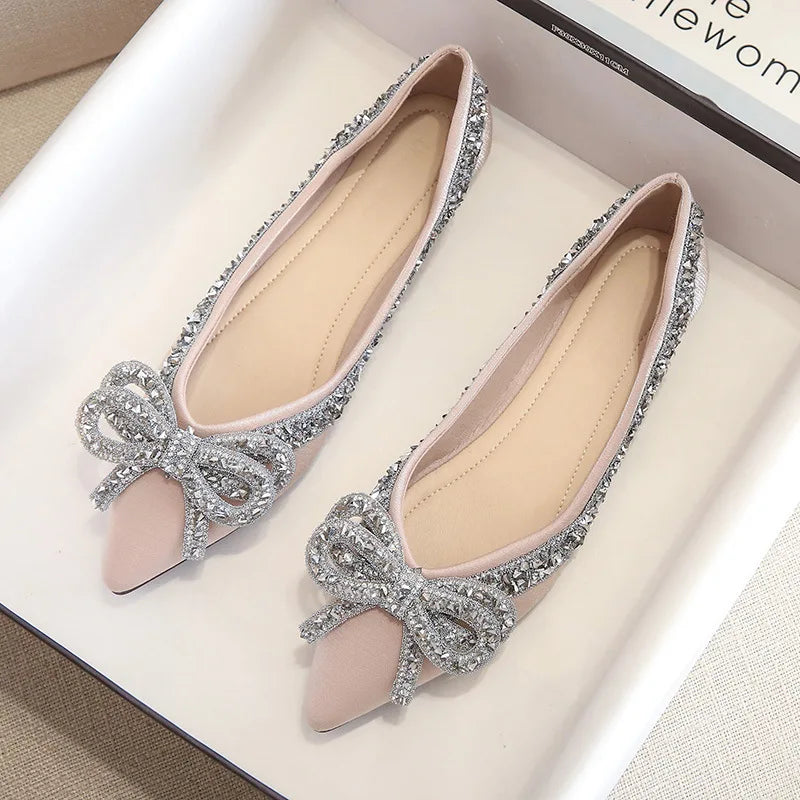 Elegant pink flats adorned with sparkling silver embellishments and large bow accents, displayed in an open box on a white surface.