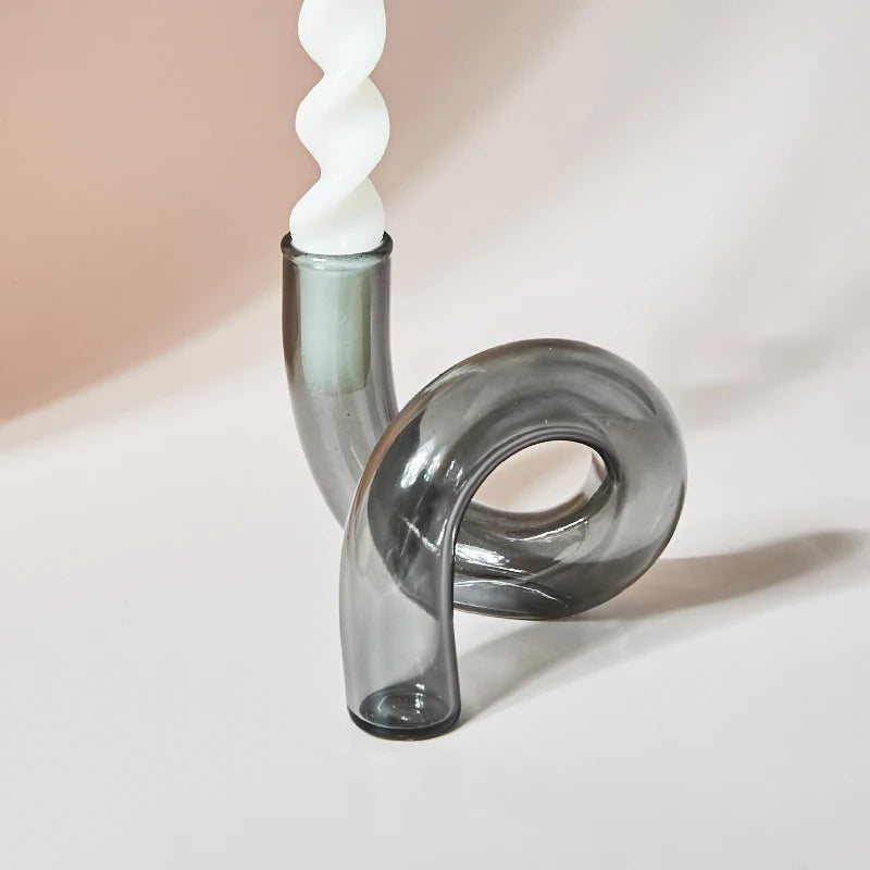 A twisted white candle sits in a modern, curvy gray glass holder against a soft, neutral background.