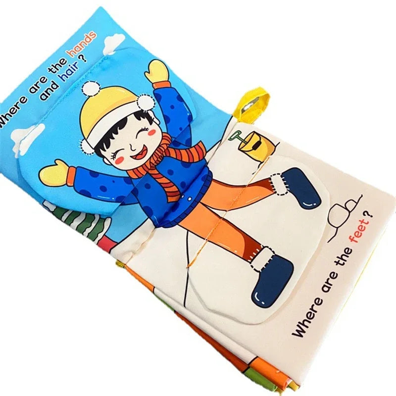 Cloth book page showing a cartoon child in winter attire. Text asks, "Where are the hands and hair?" and "Where are the feet?" along with interactive flaps.