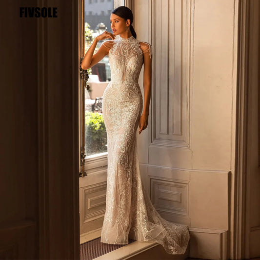 A woman in an elegant, form-fitting lace wedding gown stands by a window in a sunlit room, showcasing intricate embroidery and a high neckline.