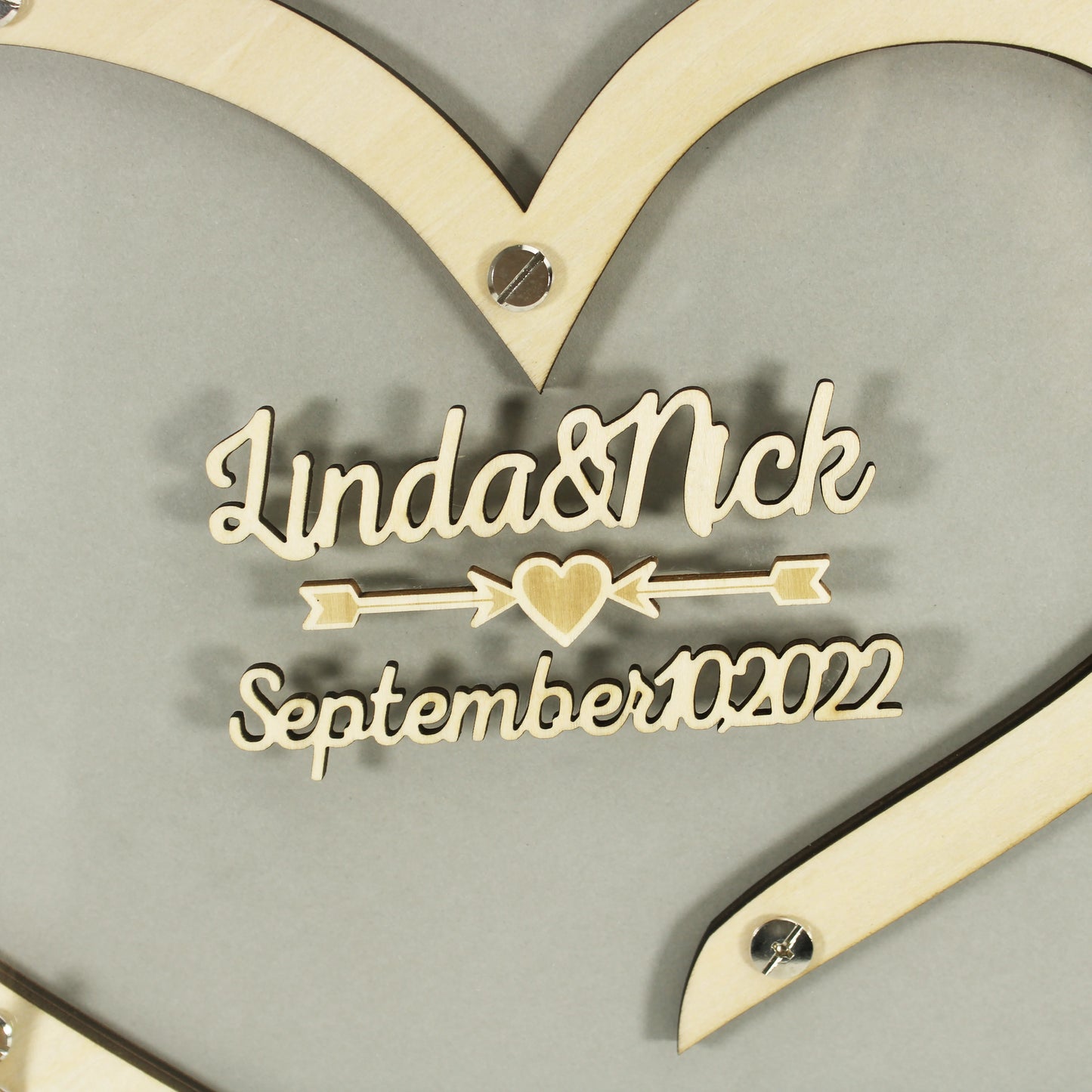 Wooden heart decoration engraved with "Linda & Nick" and "September 10, 2022," featuring an arrow and heart motif.