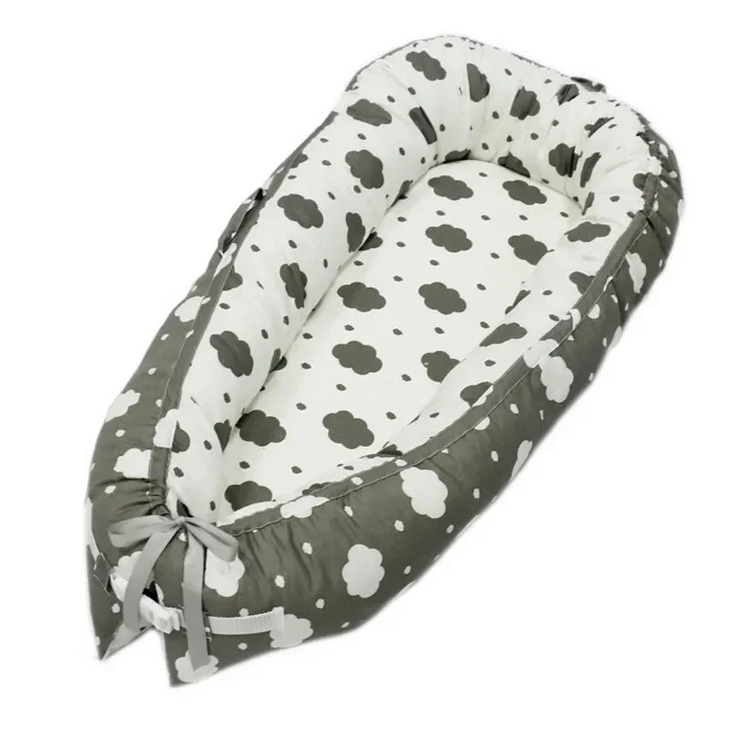 Cozy baby nest with cloud patterns in grey and white. The padded, oval-shaped bed features a tie at the end, offering a snug and secure environment for infants.