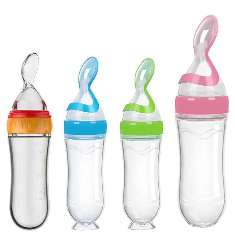 Four baby feeding bottles with silicone spoons, featuring colorful lids in red, blue, green, and pink. Each is designed with a squeezable body and stands upright.