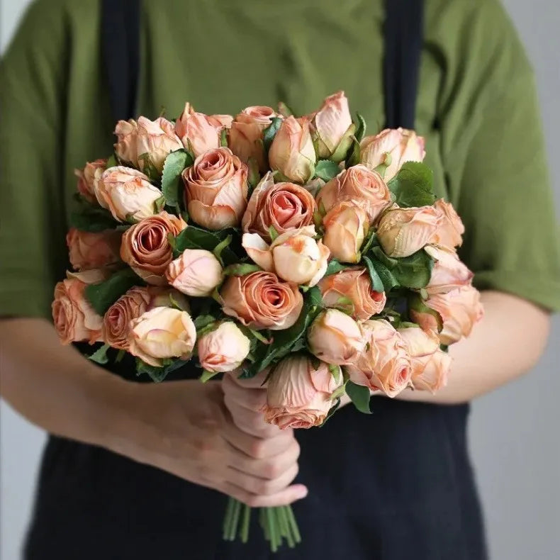 A person in a green shirt holds a large bouquet of peach-colored roses with lush green leaves, creating a vibrant contrast.