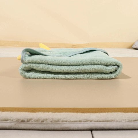 A neatly folded mint green towel rests on a beige foam mat, against a light background. A small yellow fabric detail is visible at the towel's corner, adding a hint of contrast.