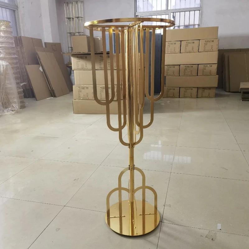 Gold metal stand with an abstract, symmetrical design, standing in a room with stacked cardboard boxes and tiled flooring.
