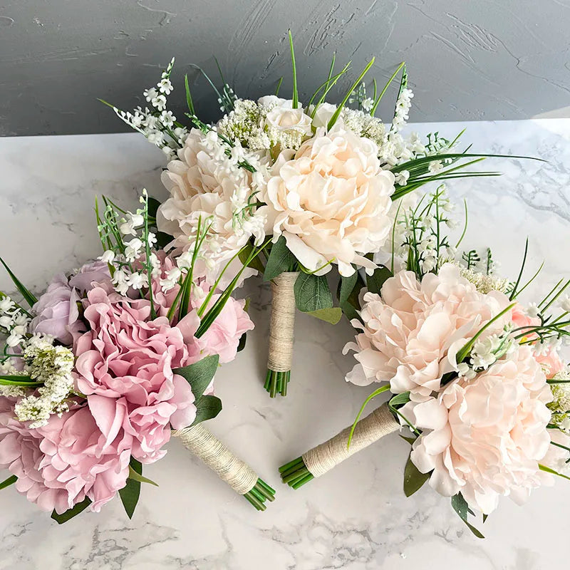 Three elegant bouquets with soft pink and white flowers, accented by green leaves and delicate white blossoms, arranged on a marble surface against a textured gray background.