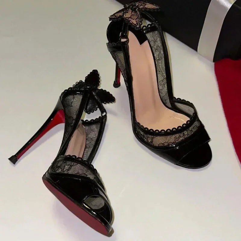 Elegant black high heels with lace detailing, peep-toe design, and butterfly accents. The shoes have a glossy finish and distinct red soles, set on a light background.