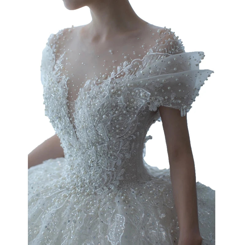 A close-up of an elegant white wedding dress featuring intricate beading and lace embellishments, with a deep V-neckline and detailed off-shoulder sleeves.