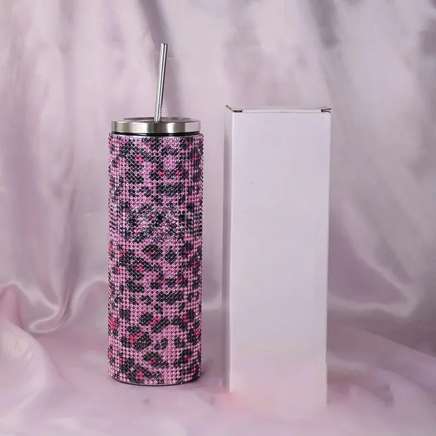 A tall tumbler with a pink leopard print design, featuring rhinestones and a metal straw, stands beside a plain white box on a soft, silky pink background.