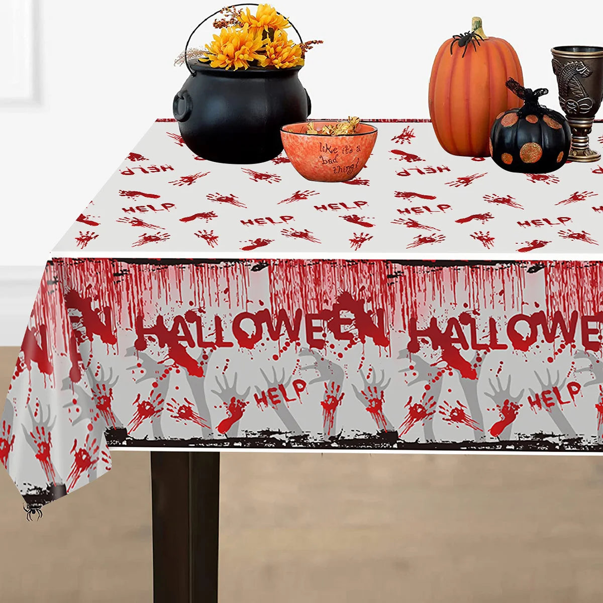 Halloween-themed tablecloth with red bloody handprints and "HELP" text, decorated with pumpkins, a cauldron, and sunflowers.