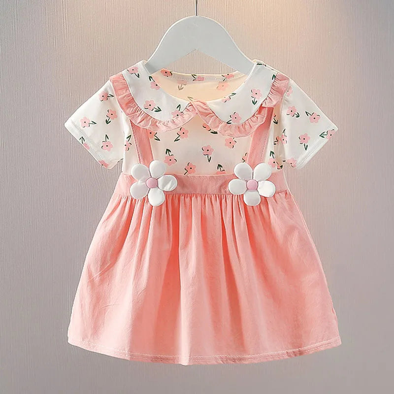 Pink toddler dress with a floral-patterned white top, Peter Pan collar, and suspender-style skirt adorned with daisy appliques, hanging on a white hanger.