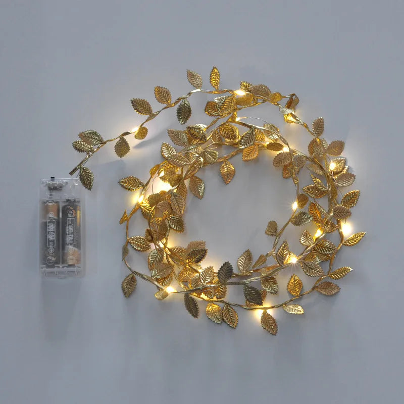 Battery-operated fairy lights with gold leaf decorations are arranged in a circular shape on a gray background.