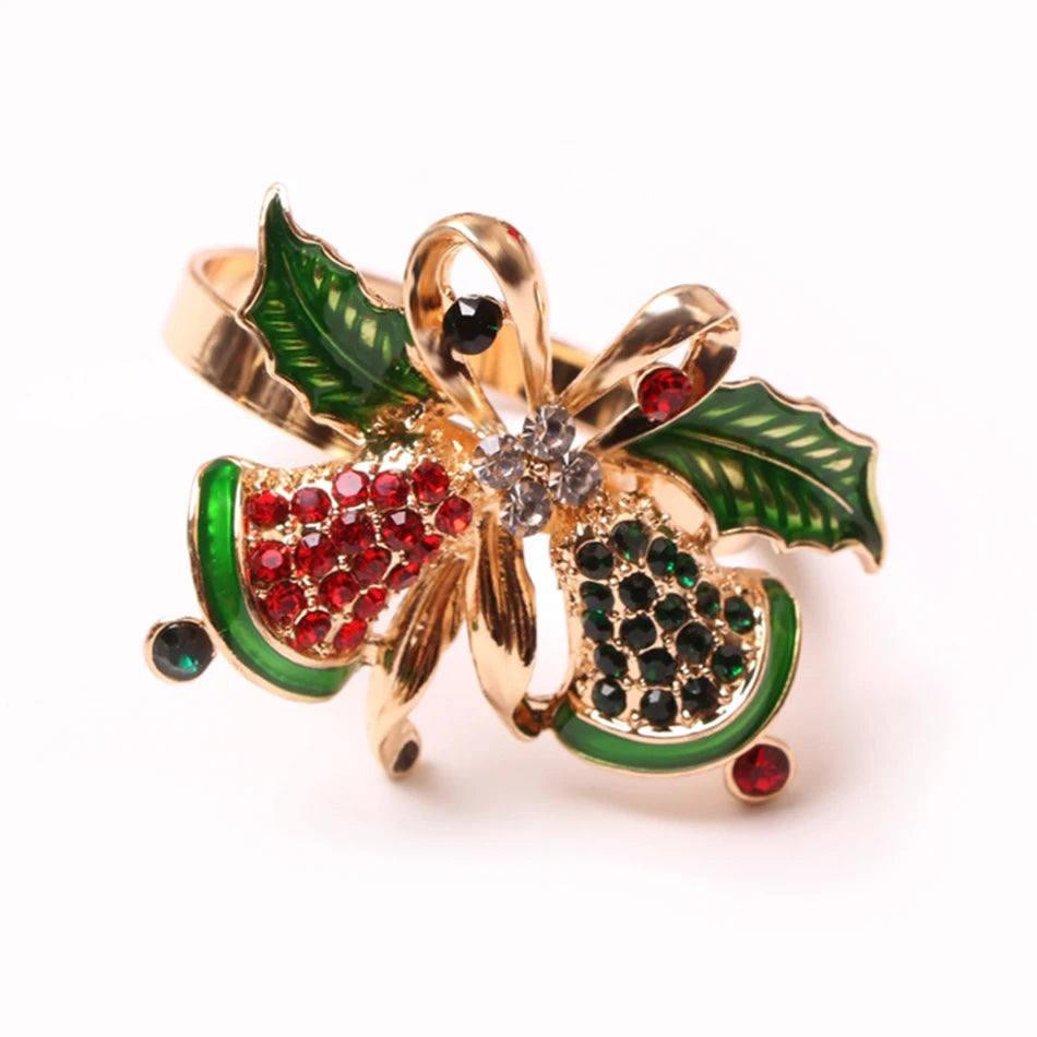 Festive holiday pin with gold ribbon, green holly leaves, and red and green gem-studded bells, embellished with sparkling crystals on a white background.