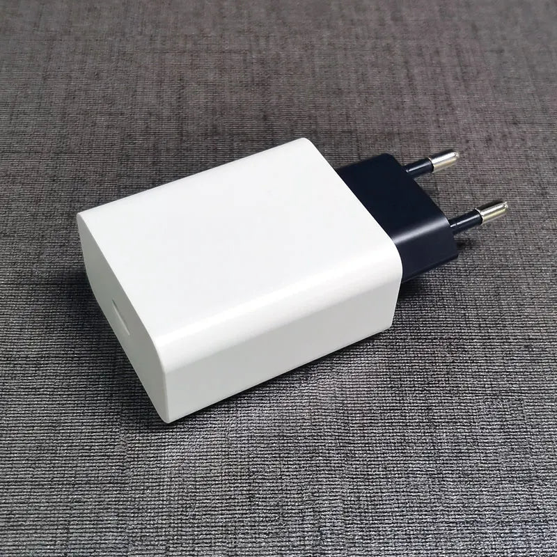 A white rectangular USB wall charger with two round prongs, lying on a gray textured surface.