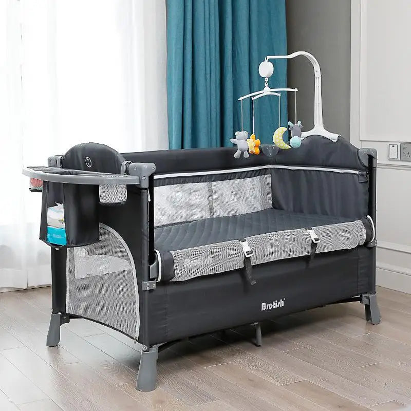 Black and gray playpen with mesh sides, attached storage pockets, and a colorful hanging mobile featuring plush toys. Placed on wooden floor near teal curtain.