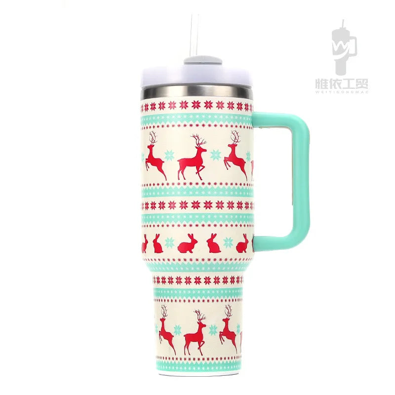 White insulated tumbler with teal handle features red reindeer and snowflake patterns. Topped with a gray lid and straw, adorned with festive green accents.