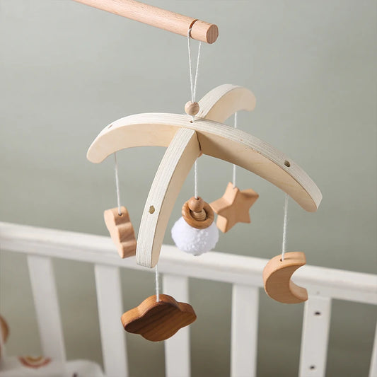 Wooden baby mobile with hanging shapes, including a cloud, star, and moon, over a white crib. The mobile features neutral tones and a minimalist design.