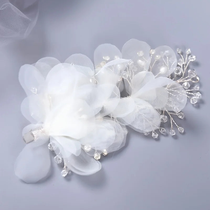 Delicate floral hair accessory with sheer white petals and small pearl-like beads on a light gray background.