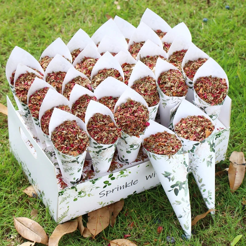 Cones filled with dried petals are neatly arranged in a decorative box on a grassy lawn. The cones have a green leaf design, and the box reads "Sprinkle with love."