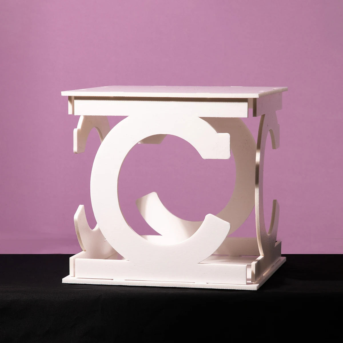 White side table with intricate, layered, circular cutout design on the sides. Set against a purple background on a black surface.