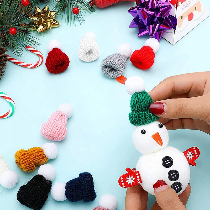 A person decorates a small snowman figure with a green knitted hat. Surrounding are colorful knitted hats, Christmas decor, candy canes, and a festive gift box.
