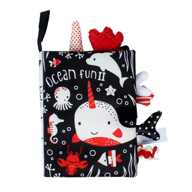 Soft baby cloth book titled "Ocean Fun II" with a narwhal, dolphin, octopus, seahorse, crab, and fish. It features black, white, and red colors with textured tabs.