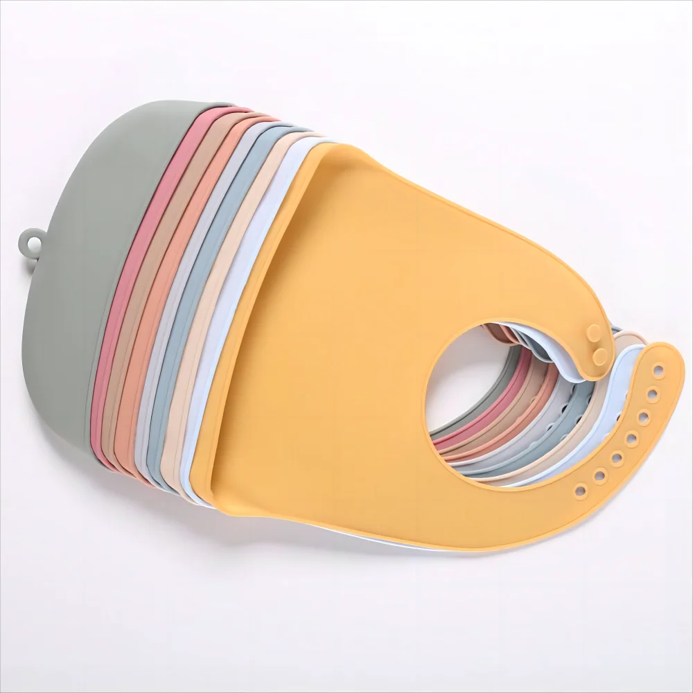 Stack of silicone bibs in various pastel colors, including yellow, green, pink, and blue, each with adjustable snap closures, arranged in a fan shape on a white background.