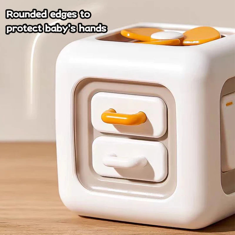 White cube-shaped toy with rounded edges features two orange and white handles and a propeller on top. Text reads: "Rounded edges to protect baby's hands."