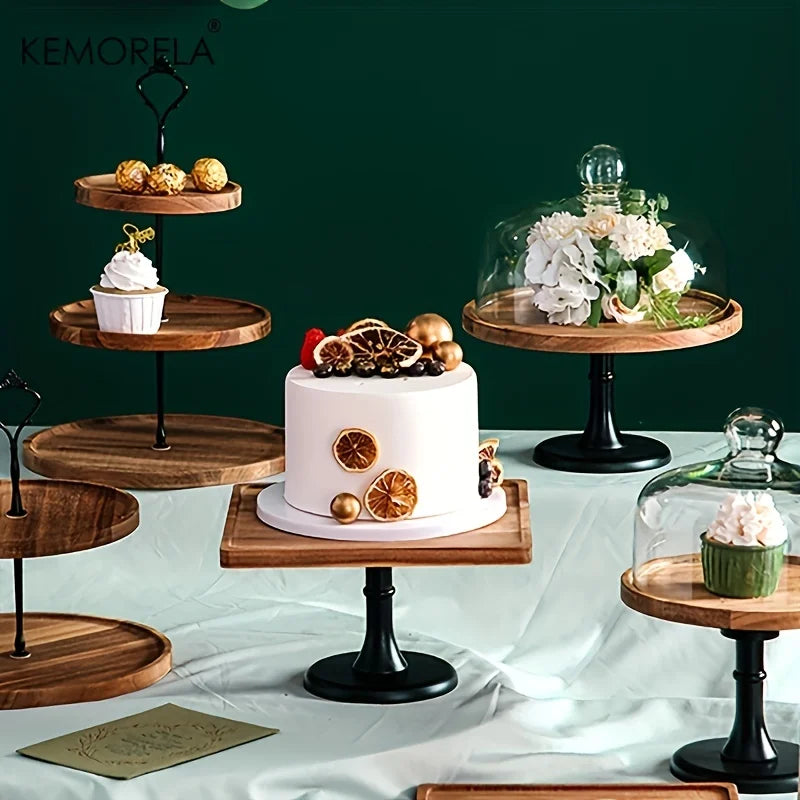 A variety of elegant wooden cake stands display a white cake with dried citrus, a cupcake, flowers under glass domes, and truffles against a dark green background.