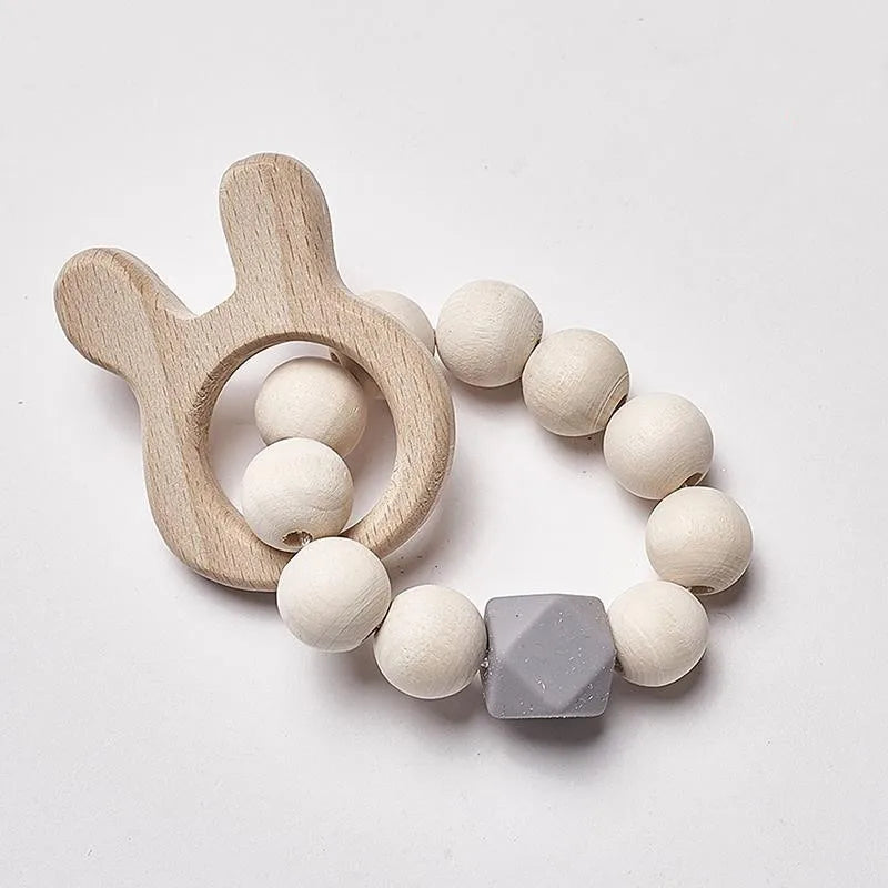 Wooden teething ring with a bunny-shaped handle, strung with white round beads and a single gray hexagonal bead, on a white background.
