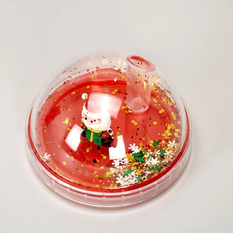 A clear drinking cup lid with a festive design features a small Santa figurine inside, surrounded by gold and white glitter, with a straw hole at the top.