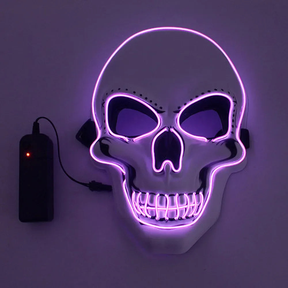 A glowing skull mask with purple LED outlining, showing hollow eyes and a smiling mouth, connected to a black battery pack with a red indicator light on.