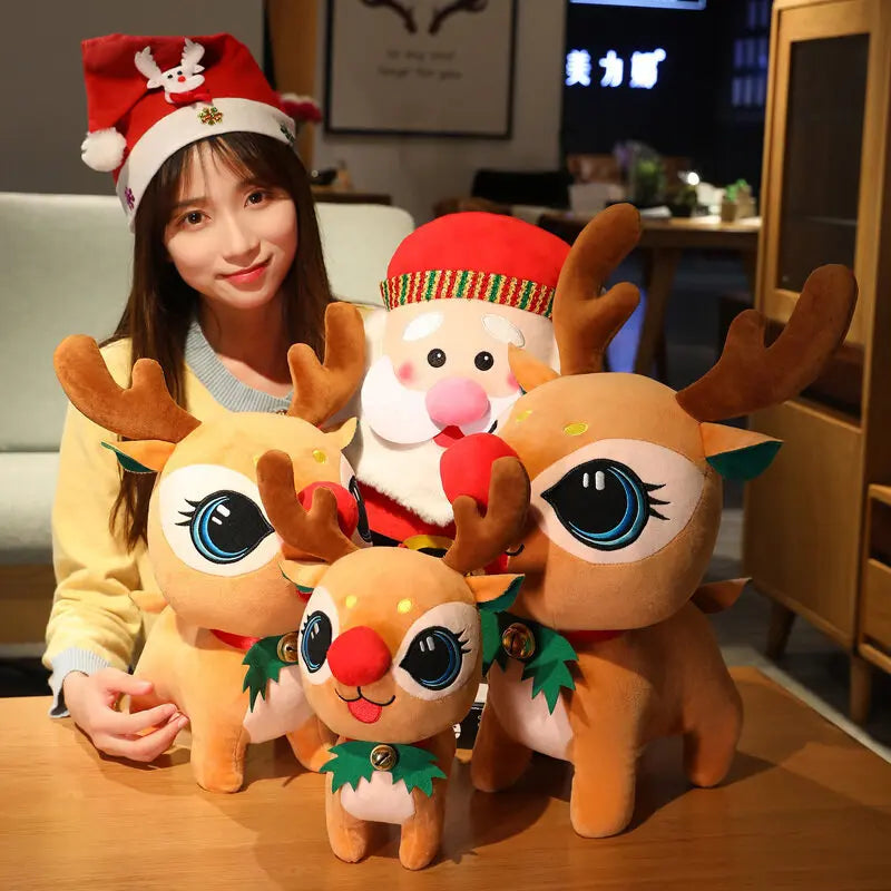 A woman wearing a festive Santa hat smiles while surrounded by multiple plush toys, including a Santa and several reindeer with large eyes and antlers, on a wooden table.